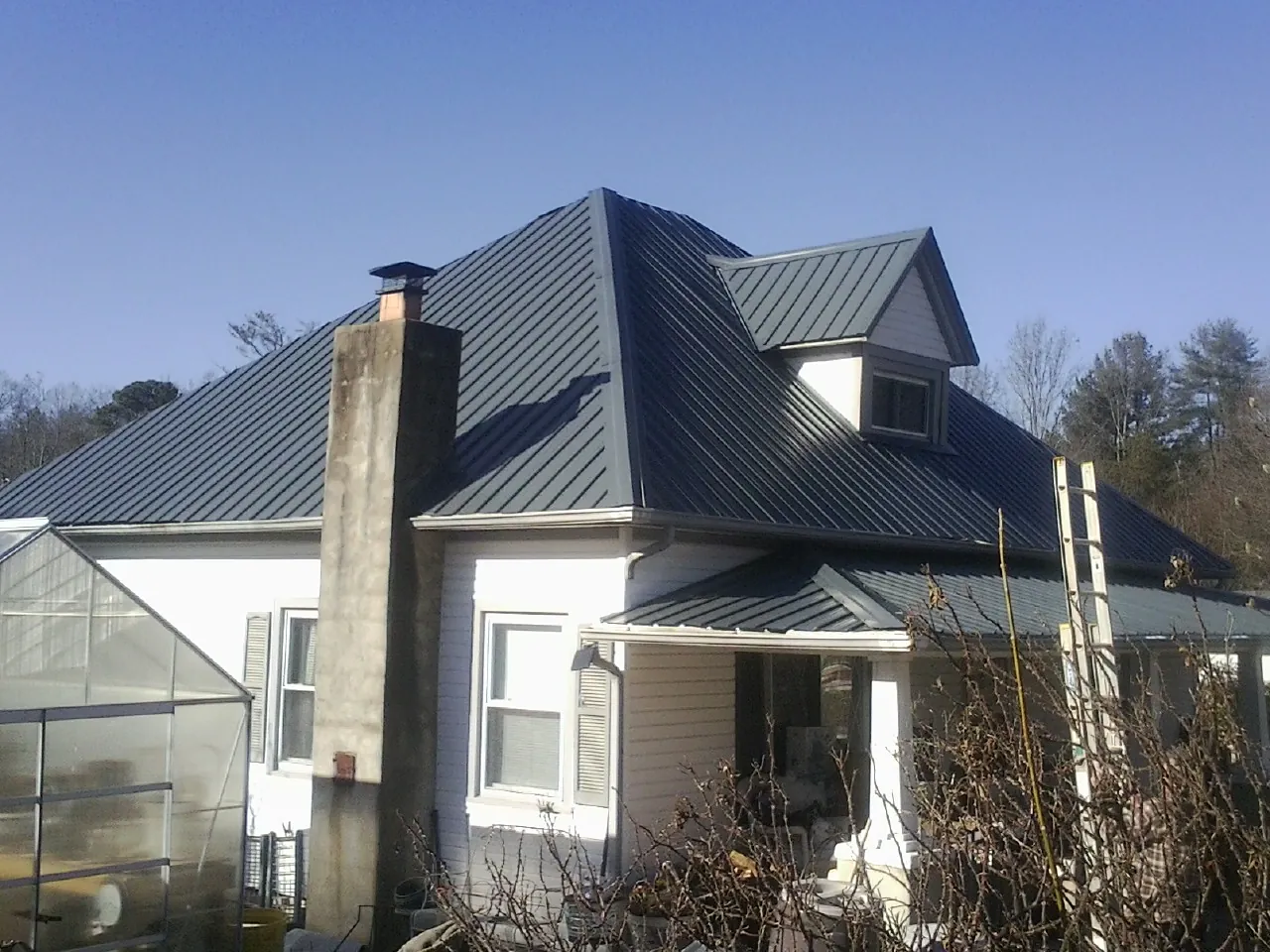 Dark blue standing seam metal roof on a white farmhouse with dormer — Slate & Tile Roof Repair by Roofing Brothers in Bonfield