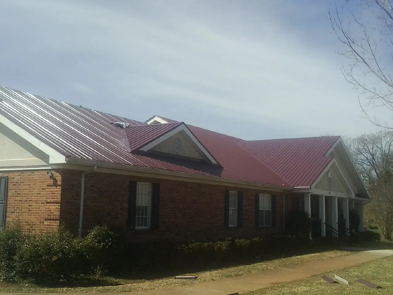 Red metal roof with gabled entries on a long brick building, from a Hail Damage Roof Repair job in Bonfield