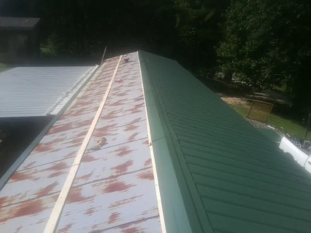 Old rusted panels beside newly installed green metal roofing — Wind Damage Roof Repair by Roofing Brothers in Bonfield