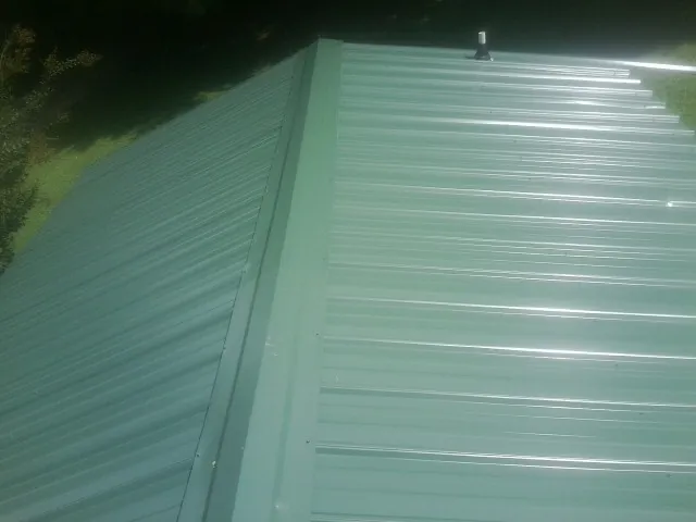 New green metal panels meeting at the ridge of a roof — Flat Roof Repair work by our crew in Bonfield