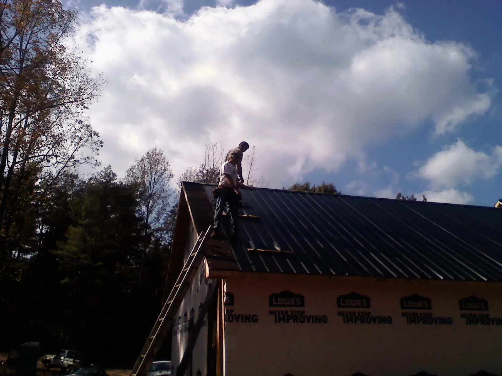 Roofer fastening dark metal panels high against a cloudy sky, from a Roof Inspection job in Bonfield