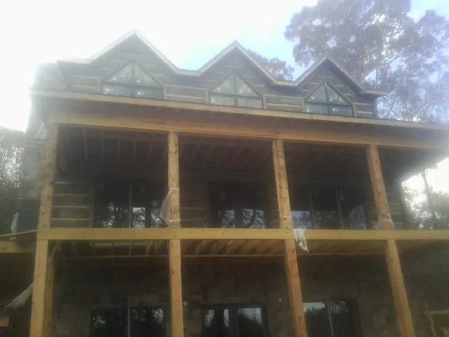 Dormers and porch framing on a large log home under construction — Roof Coating work by our crew in Bonfield