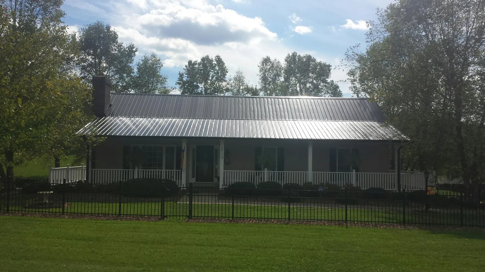 Gray metal roof on a brick ranch with a full width front porch — Gutter Guard Installation work by our crew in Bonfield