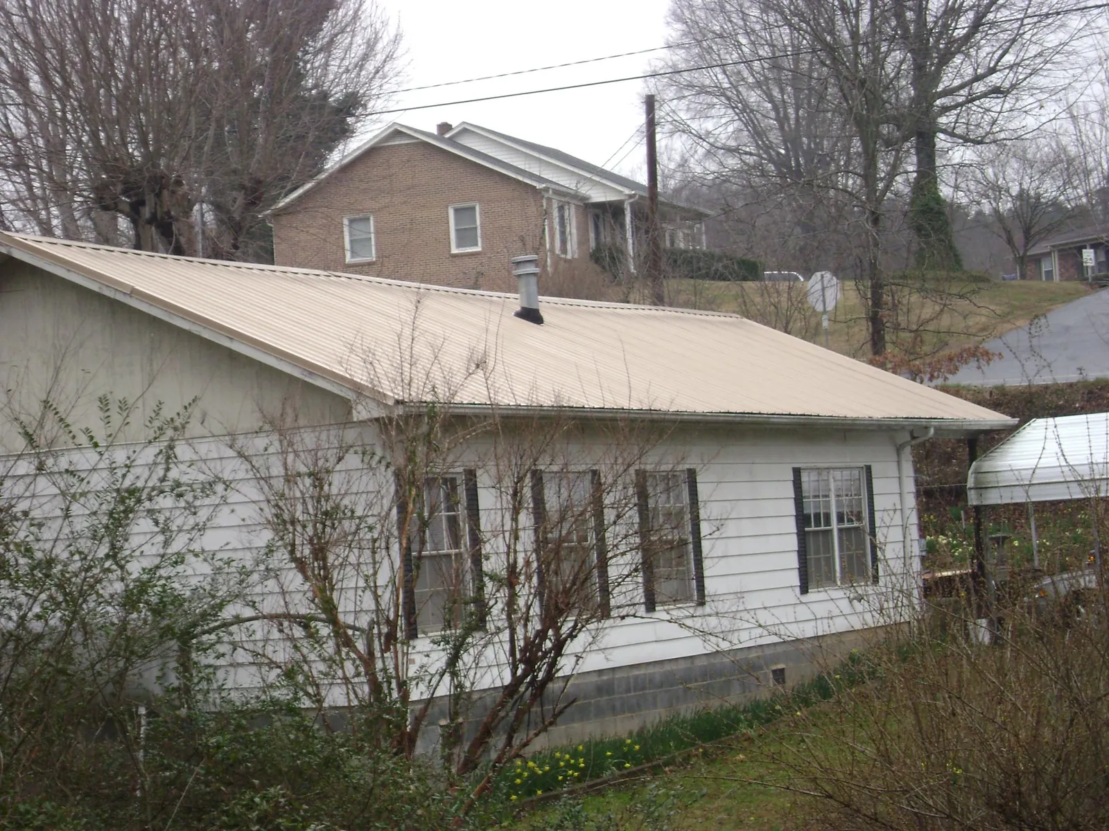Tan metal roof on a white sided house set into a hillside — Commercial Roofing by Roofing Brothers in Bonfield
