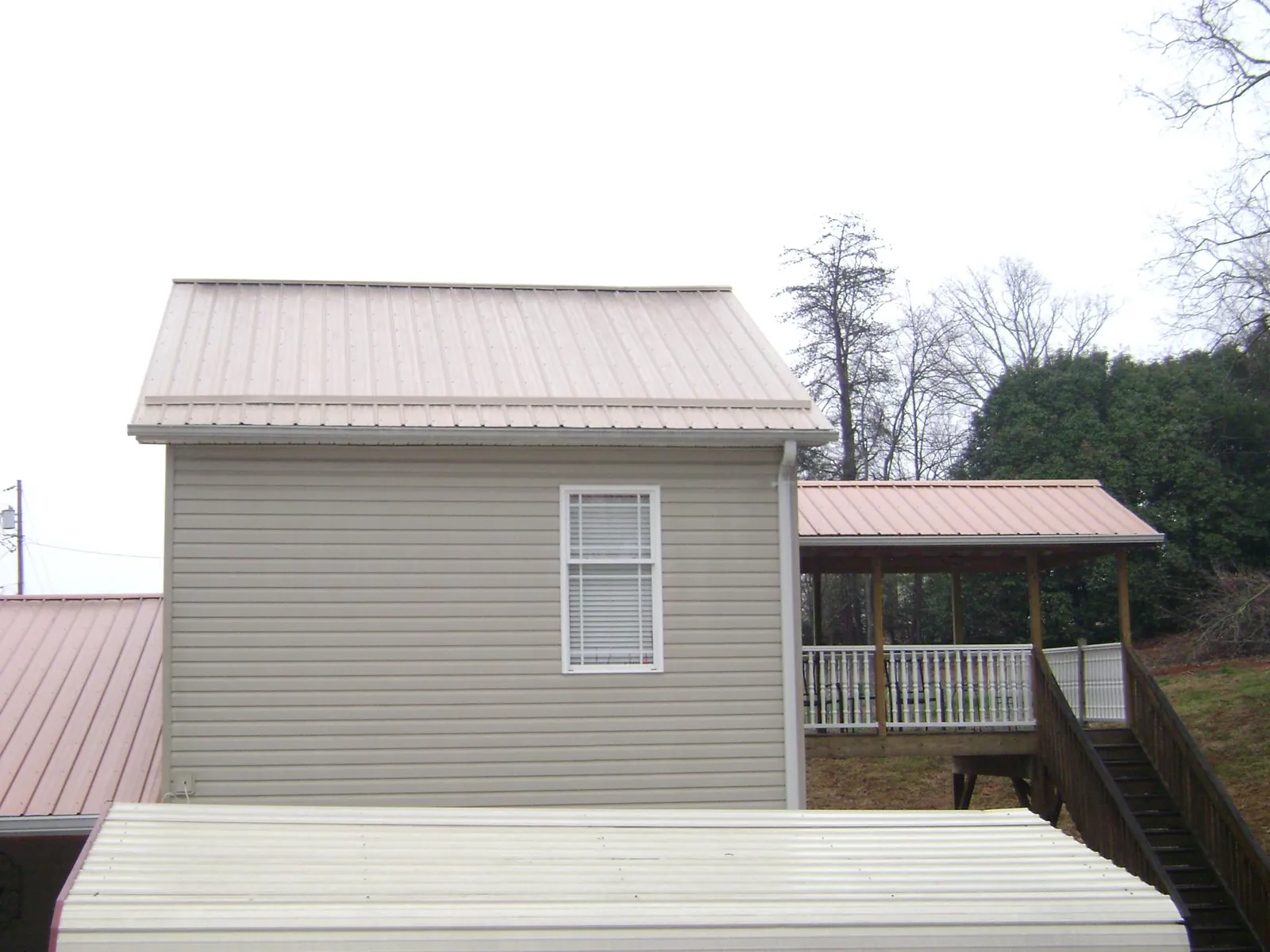 Tan metal roofs on a two story addition and attached porch, from a Roof Replacement job in Bonfield